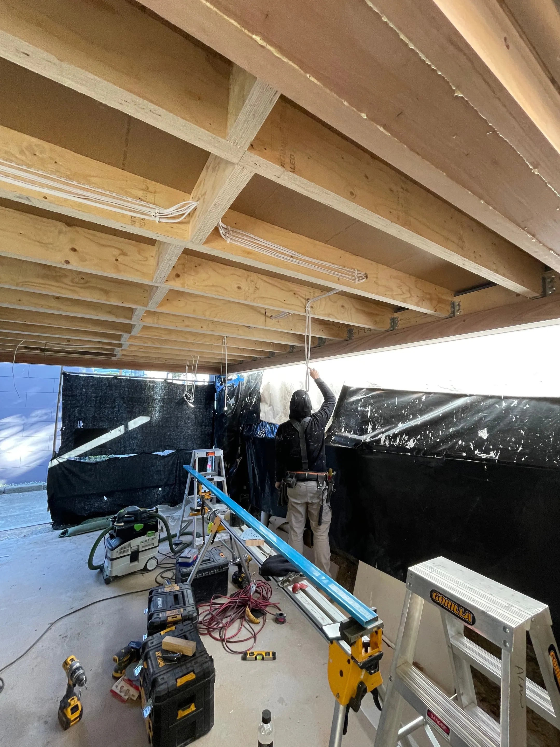 Electrician running cabling under the deck framing during rough-in at the Collaroy renovation